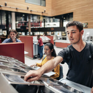 A young man reaches into a cutlery tray in a canteen.
