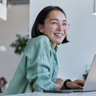 Young woman sits at her laptop and looks into the distance with a smile.
