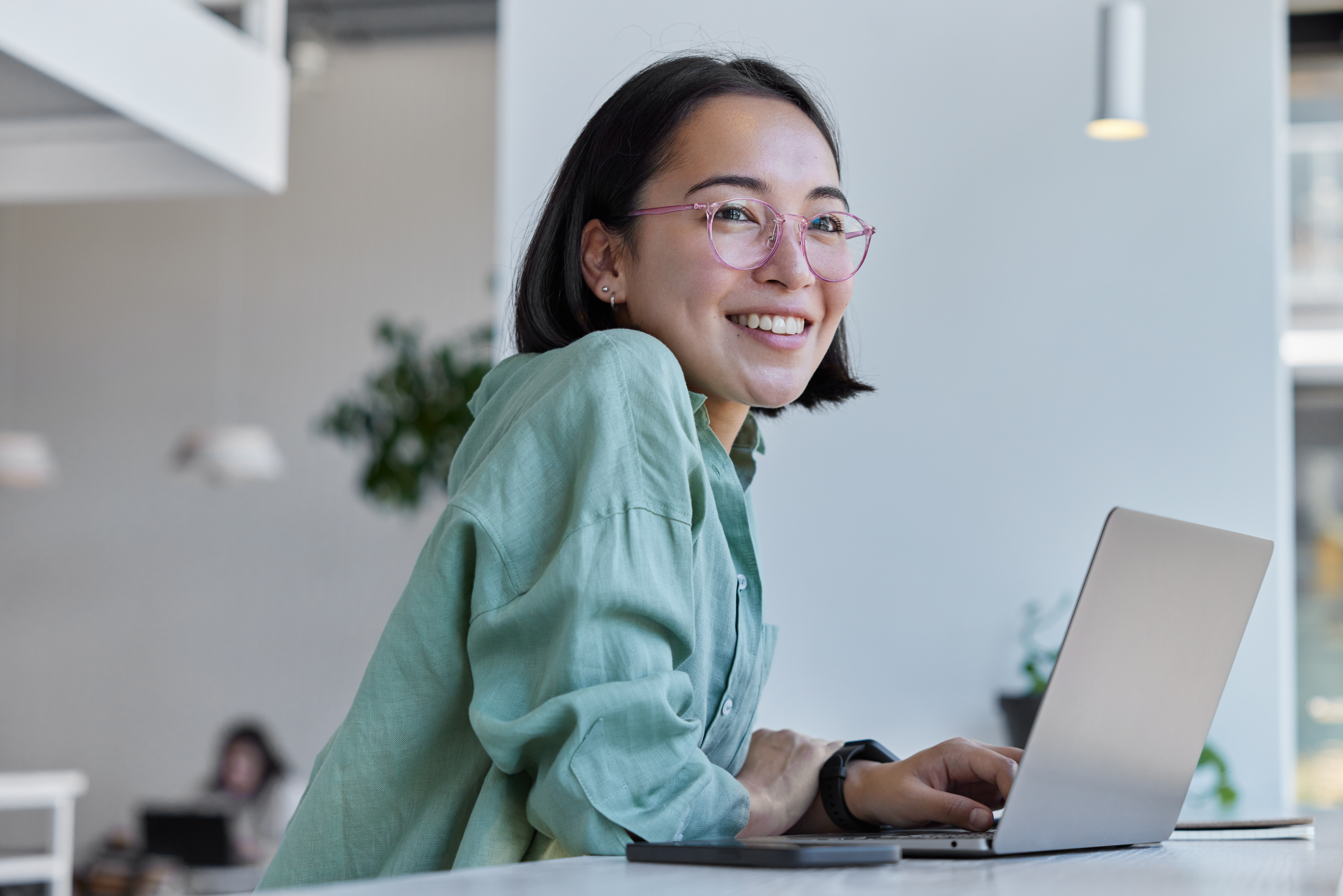 Young woman sits at her laptop and looks into the distance with a smile.