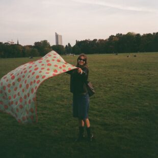 A young woman stands with a picnic blanket in a park in Leipzig.