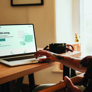 Young person sitting at a desk and working on a laptop. The BAföG Digital website is open.